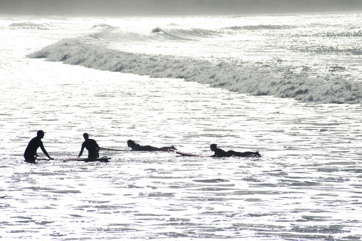 Silhouettes of surfers on their surfboards waiting for a wave on sunlit water with two kneeling and two lying flat on their boards