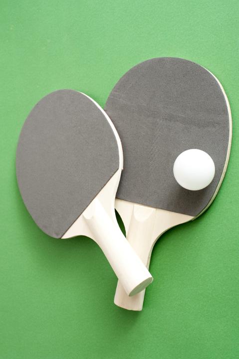 Table tennis bats and a ball lying on the green wooden table read for a game of indoor ping pong or table tennis