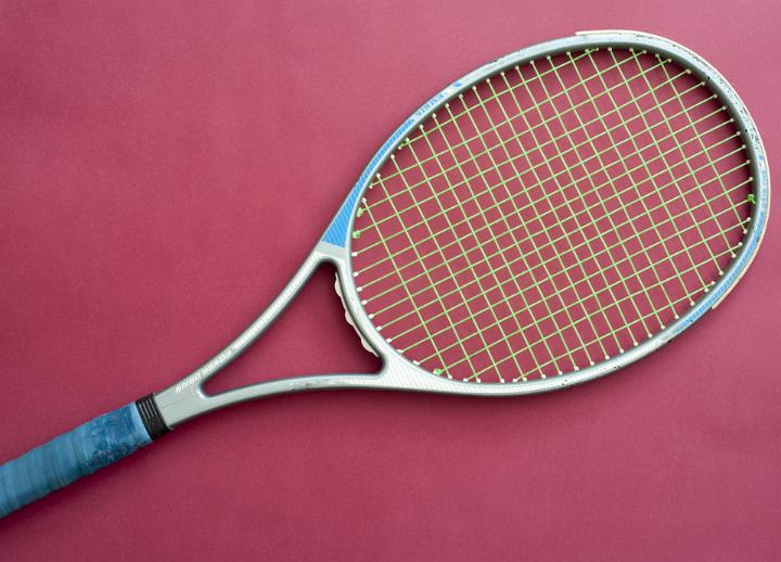 Modern metal frame tennis racket lying diagonally across the frame on a magenta background showing string detail