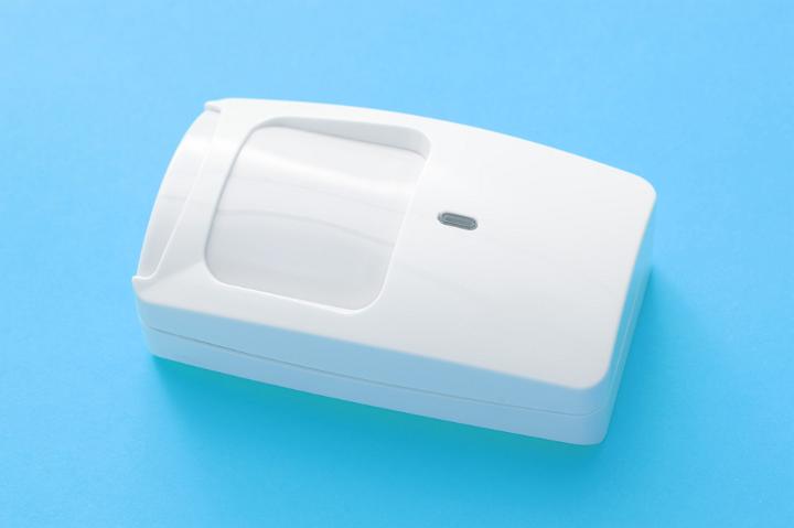 White plastic infrared motion sensor for an alarm system for a building interior lying on a turquoise blue background