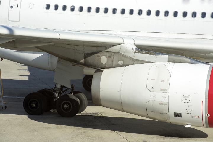 A close up, abstract crop of an airliner plane wing, landing gear an carriage on a concrete runway.
