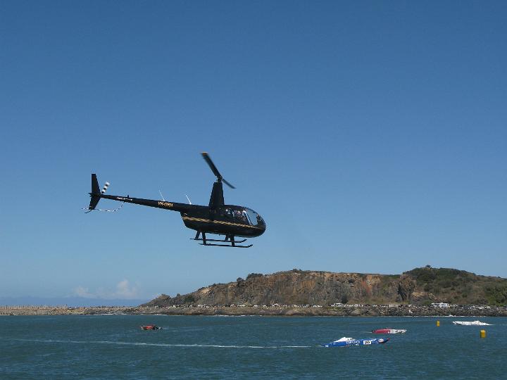Side view of a helicopter in flight over the ocean approaching the shoreline against a clear blue sunny sky