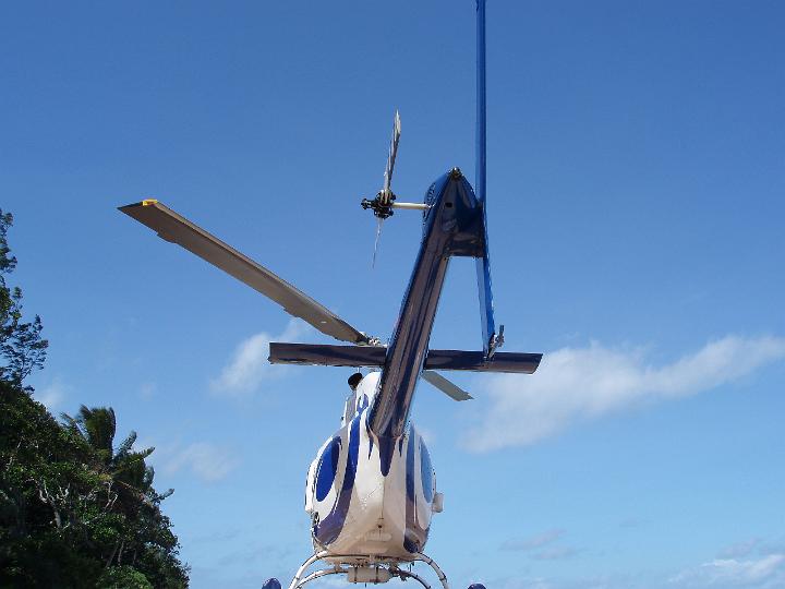 Rear low angle view of a parked helicopter showing the rotary blade on the tail and overhead rotor for lift against a clear blue sky