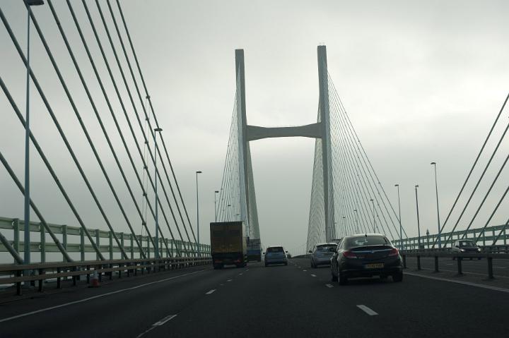 Traffic on a highway bridge at a motorway crossing on a dark overcast day with high tension suspension cables on either side