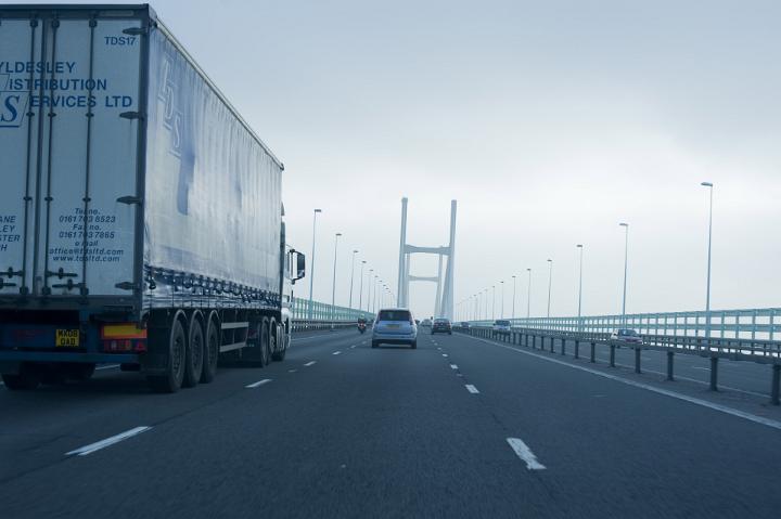 Large haulage truck travelling on a motorway bridge or traffic crossing viewed from a car driving alongside on a cold rainy grey day with copy space