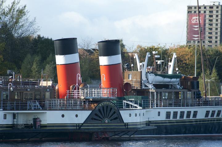 Bright red funnels on an old riverboat paddle steamer on a river with a modern high rise building visible behind