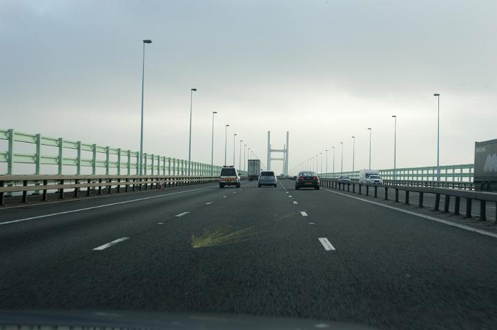Cars and trucks disappear into the distance on a busy motorway under a dull, overcast and stormy winter sky