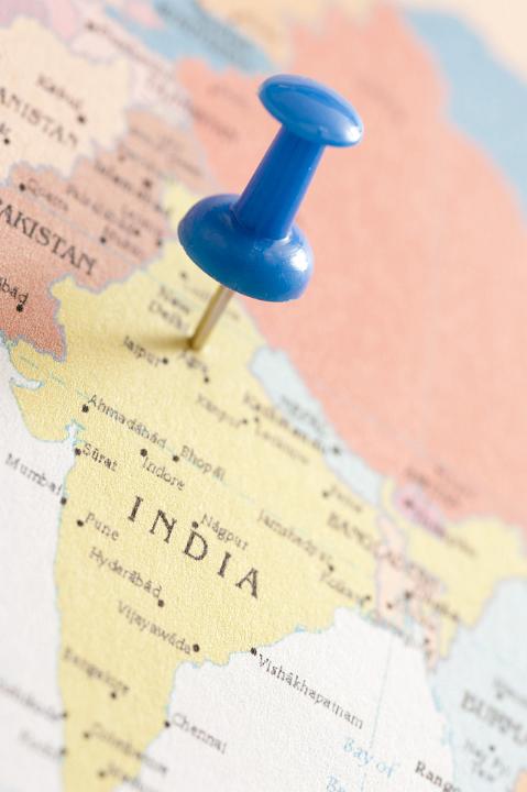 Close Up of Blue Thumb Tack Pinned into Map of India Marking Location of New Delhi