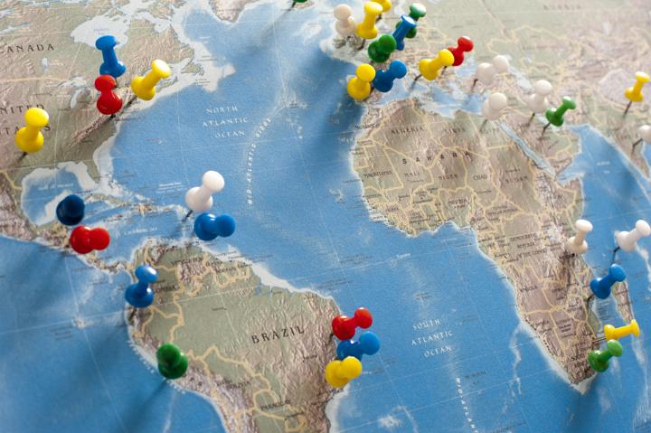Multi-Colored Pins Tacked into Various Locations and Destinations on Flat Map of the World in Trip Planning Concept Image