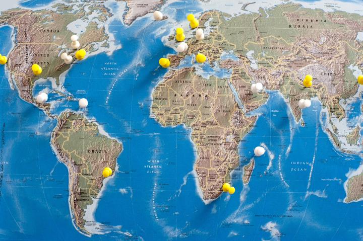 Yellow and White Thumb Tacks Pinned into Various Locations on Map of the World as if Planning a Trip